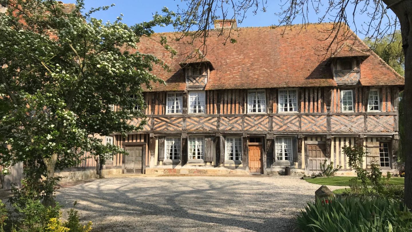 La façade du logis vue depuis la cour : pans de bois et briques disposées en chevrons, portes et volets de bois.